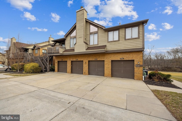 view of front of property with brick siding, a chimney, concrete driveway, an attached garage, and stairs