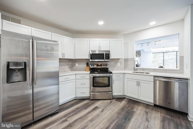 kitchen with stainless steel appliances, a sink, light countertops, decorative backsplash, and dark wood-style floors