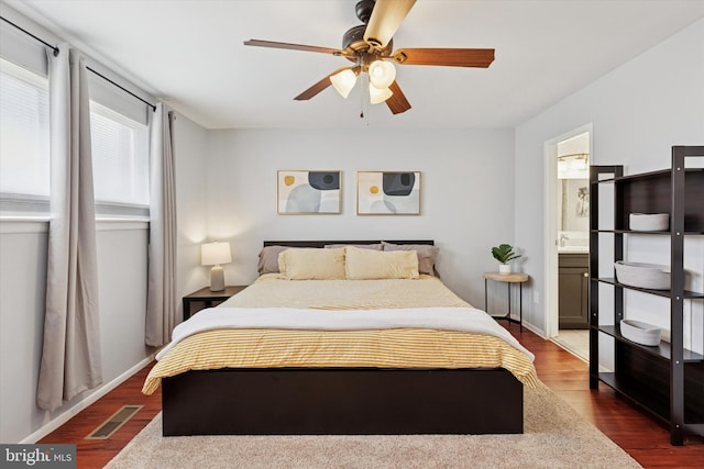 bedroom featuring baseboards, visible vents, dark wood finished floors, ceiling fan, and ensuite bathroom