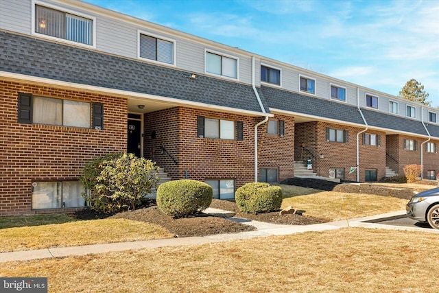 view of front facade with central AC, mansard roof, a shingled roof, and brick siding