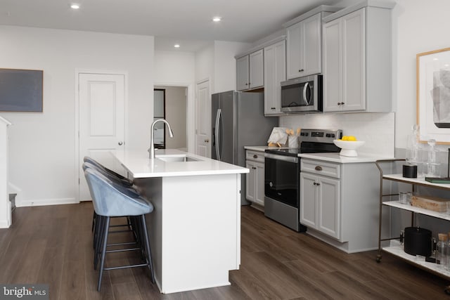 kitchen with appliances with stainless steel finishes, dark wood-style flooring, a sink, and backsplash