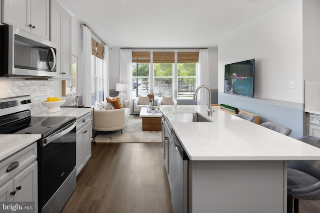 kitchen with a breakfast bar area, open floor plan, a sink, stainless steel appliances, and backsplash