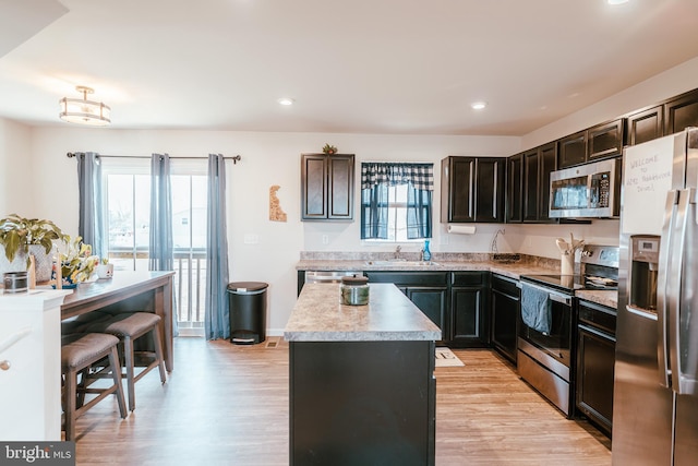 kitchen featuring a center island, light wood-type flooring, light countertops, appliances with stainless steel finishes, and a sink