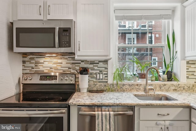 kitchen with a sink, backsplash, white cabinetry, stainless steel appliances, and light stone countertops