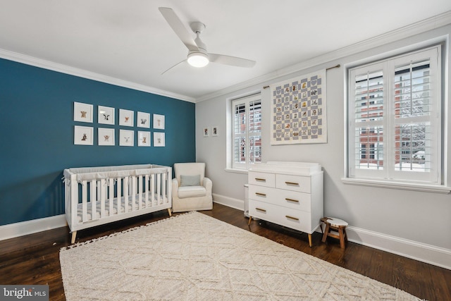 bedroom featuring baseboards, a nursery area, dark wood-style flooring, and crown molding