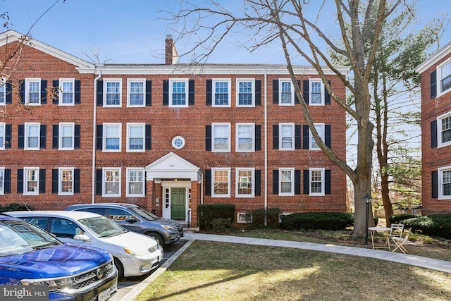 multi unit property featuring a front yard, brick siding, uncovered parking, and a chimney