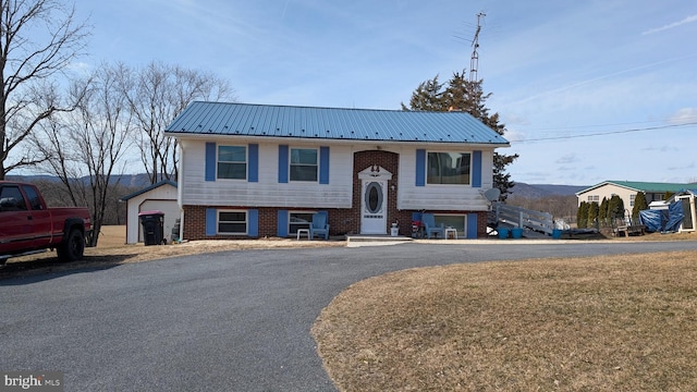 bi-level home with entry steps, brick siding, metal roof, and driveway