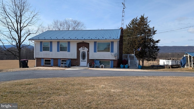 split foyer home featuring aphalt driveway, a front yard, brick siding, and metal roof