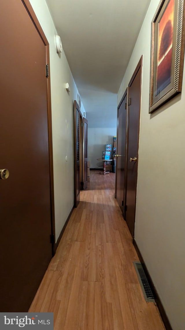 hall with visible vents, light wood-style flooring, and baseboards