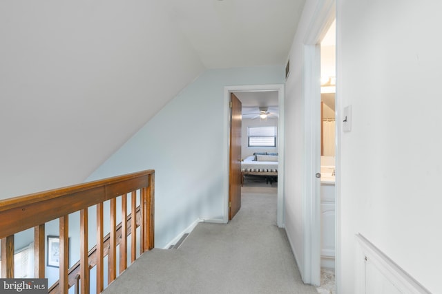 corridor featuring visible vents, vaulted ceiling, and light colored carpet