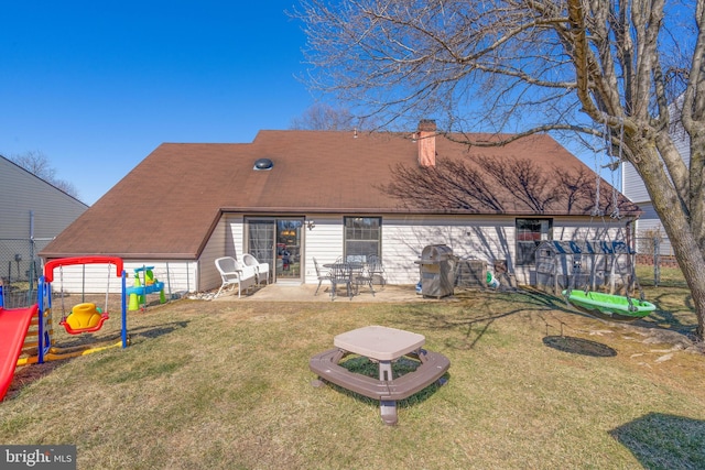 rear view of property with a chimney, fence, a yard, a patio area, and a playground