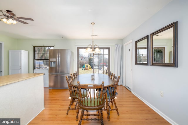 dining space with baseboards, ceiling fan with notable chandelier, light wood-type flooring, and a healthy amount of sunlight