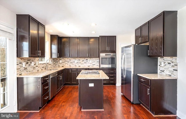 kitchen with stainless steel appliances, a sink, light stone counters, and a kitchen island