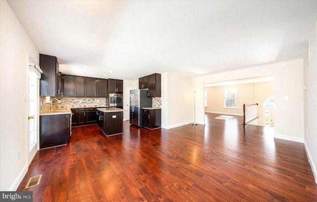 kitchen with a kitchen island, dark wood-style flooring, stainless steel appliances, dark brown cabinets, and backsplash