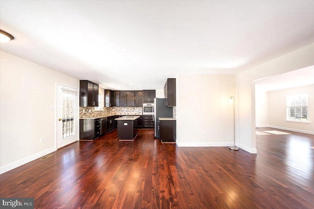 kitchen with decorative backsplash, appliances with stainless steel finishes, a center island, light countertops, and dark brown cabinets