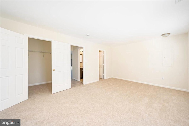 unfurnished bedroom with a spacious closet, baseboards, a closet, and light colored carpet