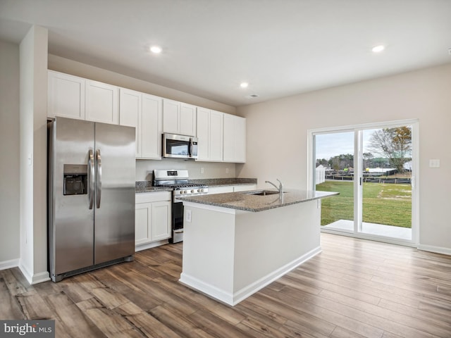 kitchen with stainless steel appliances, dark stone countertops, wood finished floors, and white cabinetry