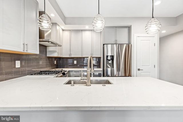 kitchen with light stone counters, backsplash, a sink, wall chimney range hood, and stainless steel fridge with ice dispenser