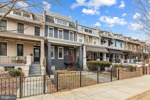 townhome / multi-family property featuring a fenced front yard, brick siding, mansard roof, covered porch, and a residential view