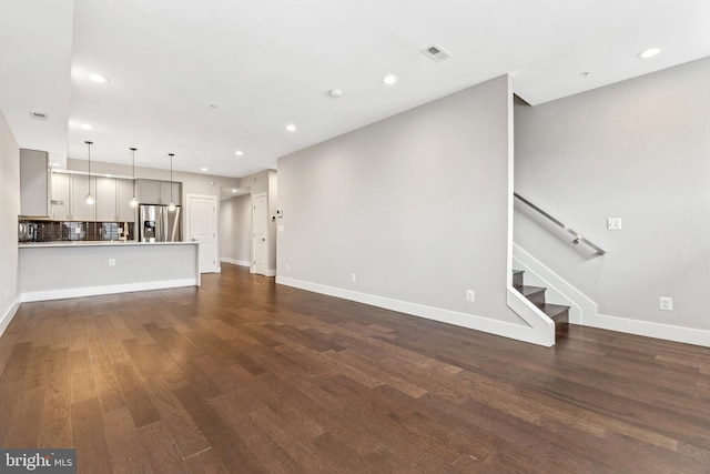 unfurnished living room with recessed lighting, visible vents, dark wood-type flooring, baseboards, and stairs