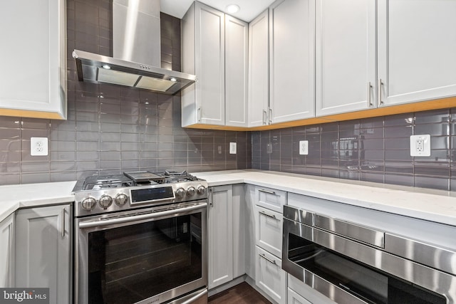 kitchen with light stone countertops, wall chimney range hood, tasteful backsplash, and appliances with stainless steel finishes