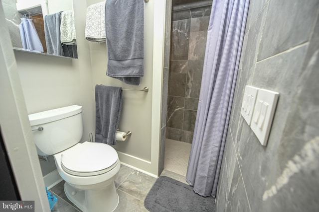 full bathroom with tile patterned flooring, baseboards, tiled shower, and toilet