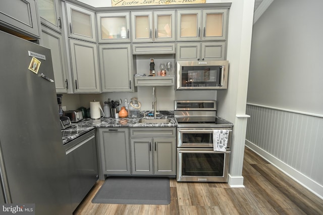 kitchen featuring gray cabinetry, stainless steel appliances, wood finished floors, and wainscoting