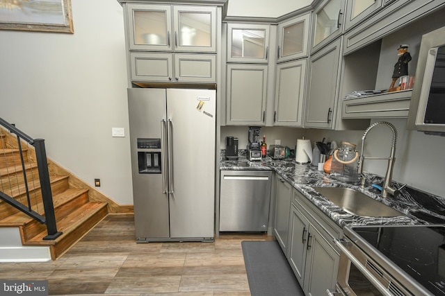 kitchen featuring a sink, light wood-style floors, appliances with stainless steel finishes, gray cabinets, and dark stone countertops