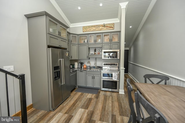 kitchen featuring a wainscoted wall, dark wood finished floors, stainless steel appliances, gray cabinetry, and ornamental molding