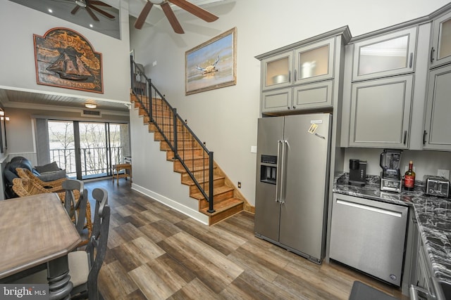 kitchen featuring stainless steel appliances, gray cabinets, glass insert cabinets, open floor plan, and wood finished floors