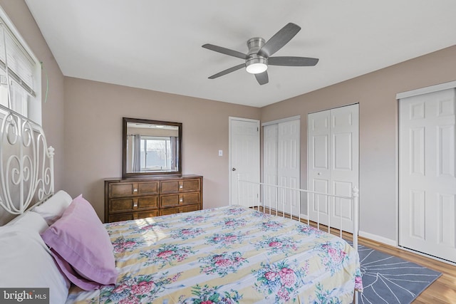 bedroom with baseboards, a ceiling fan, multiple closets, and wood finished floors