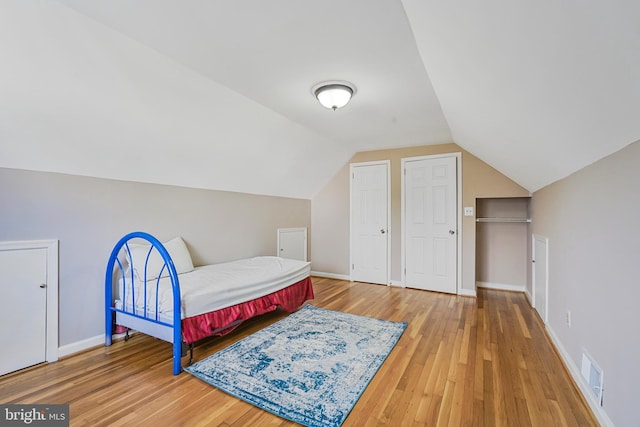 bedroom with visible vents, vaulted ceiling, baseboards, and wood finished floors