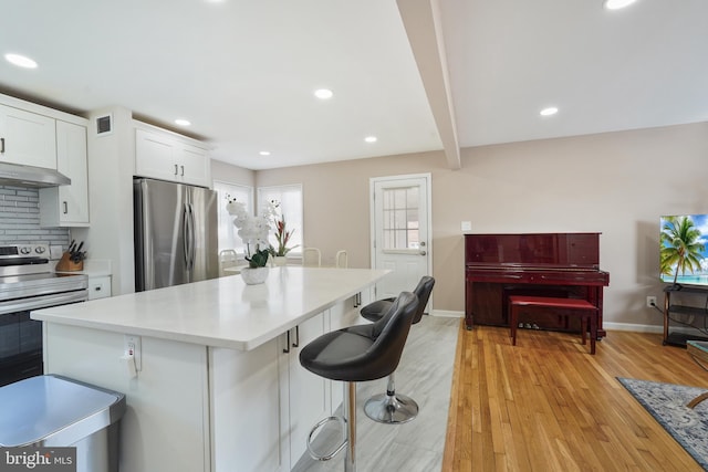 kitchen featuring a kitchen island, white cabinetry, appliances with stainless steel finishes, light wood-type flooring, and backsplash