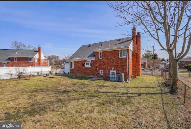 rear view of property with brick siding, a chimney, a lawn, central AC, and a fenced backyard