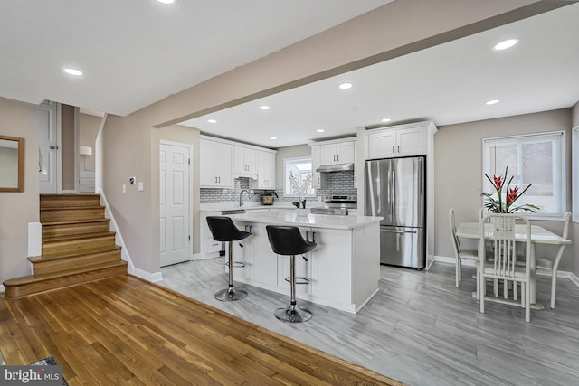 kitchen featuring a breakfast bar area, tasteful backsplash, light countertops, appliances with stainless steel finishes, and white cabinetry