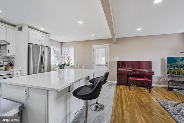 kitchen with visible vents, freestanding refrigerator, light wood-type flooring, white cabinetry, and range with electric stovetop