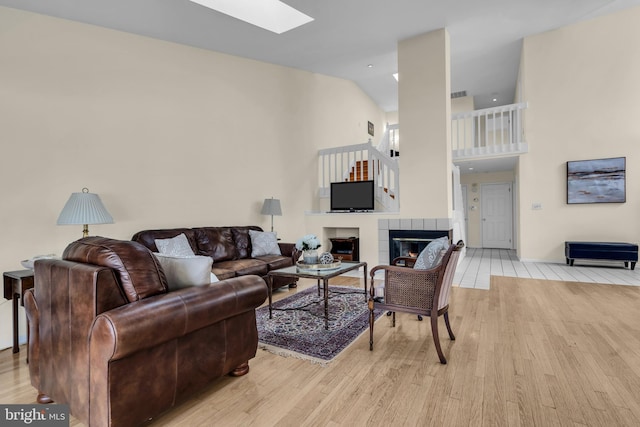 living area featuring light wood-style floors, a skylight, a fireplace, and high vaulted ceiling