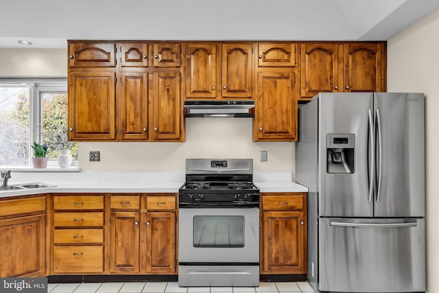 kitchen with brown cabinetry, appliances with stainless steel finishes, light countertops, under cabinet range hood, and a sink