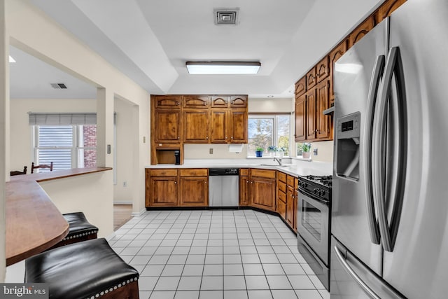 kitchen featuring light tile patterned flooring, a sink, light countertops, appliances with stainless steel finishes, and brown cabinetry