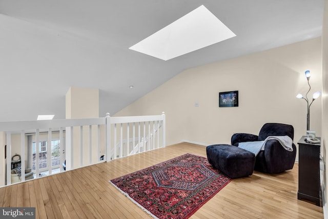 sitting room featuring lofted ceiling with skylight, an upstairs landing, and hardwood / wood-style floors