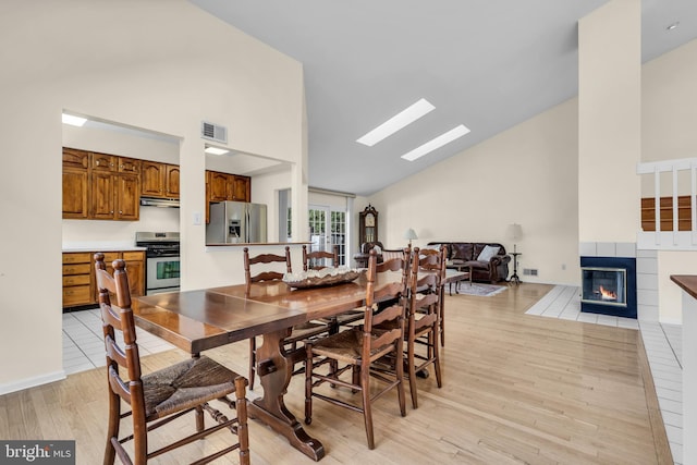 dining space with light wood-type flooring, high vaulted ceiling, a fireplace with flush hearth, and visible vents