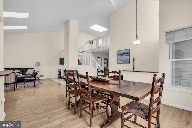 dining room featuring a skylight, light wood finished floors, stairway, high vaulted ceiling, and baseboards