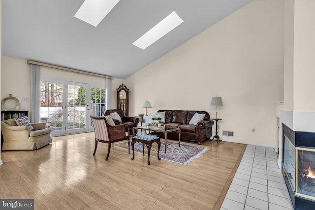 living area with a skylight, visible vents, light wood-style floors, high vaulted ceiling, and a multi sided fireplace