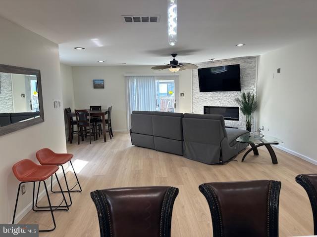 living area featuring a fireplace, wood finished floors, a ceiling fan, visible vents, and baseboards