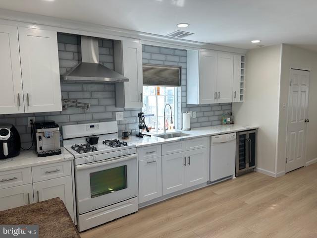 kitchen featuring white appliances, visible vents, wall chimney exhaust hood, wine cooler, and a sink