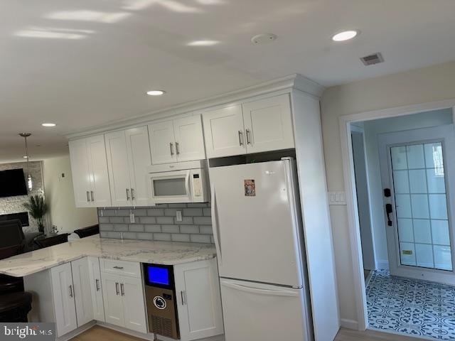 kitchen with a peninsula, white appliances, visible vents, white cabinets, and light stone countertops