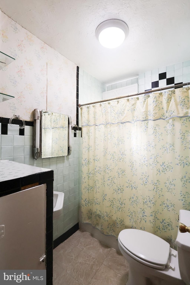 full bathroom featuring wallpapered walls, toilet, a textured ceiling, vanity, and tile walls