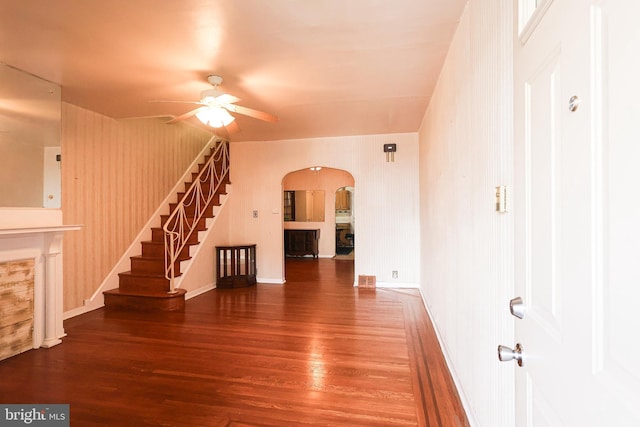 unfurnished living room featuring arched walkways, wood finished floors, a ceiling fan, baseboards, and stairs