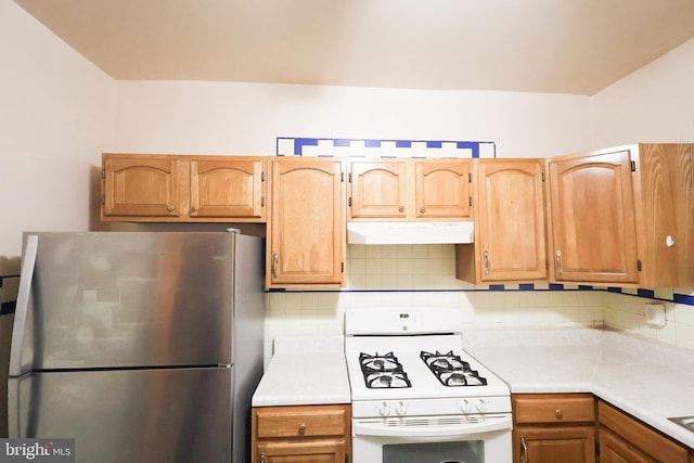 kitchen featuring decorative backsplash, freestanding refrigerator, light countertops, white gas stove, and under cabinet range hood