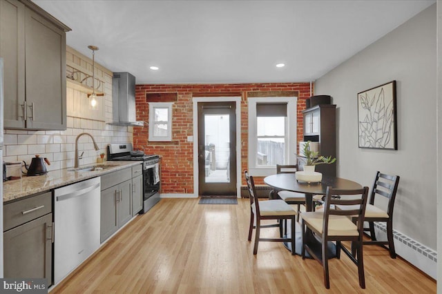 kitchen featuring stainless steel appliances, gray cabinetry, light wood-style floors, a sink, and wall chimney exhaust hood